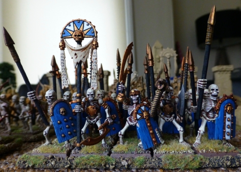 Front view of a regiment of skeletons with spears, a banner and a horn blower