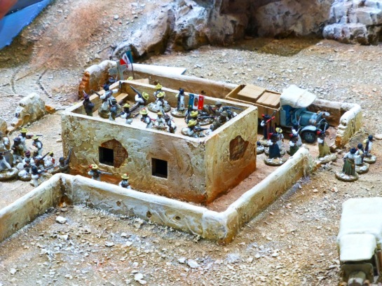 An adobe building and compound with irregular troops and two lorries