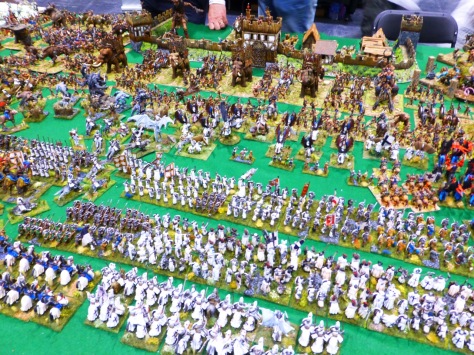Large regiments of knights and foot soldiers clad in white meeting a Barbarian horde in front of a wooden fort