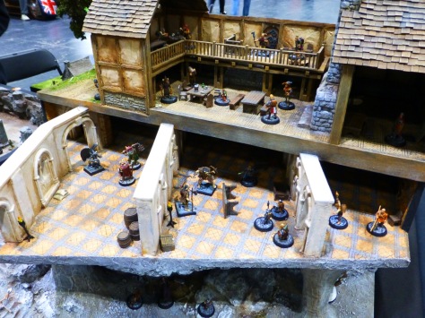 Cutaway of a medieval style house with a basement and cellar floor, all containing groups of heroes fighting against evil creatures