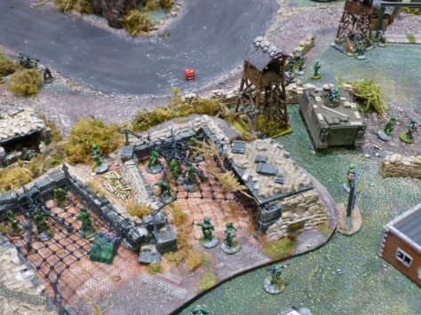 Two artillery emplacements on a river bank with a watchtower and parked APC
