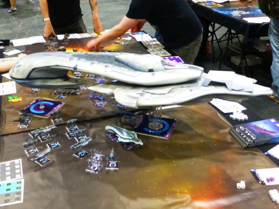 Small space ships on a star field gaming table surrounding a much larger craft