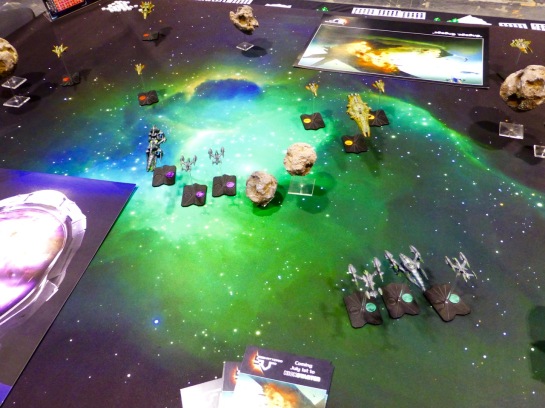 Two fleets of opposing spacecraft on a dark blue gaming table with stars and a green nebula