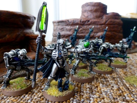Side view of a group of robot warriors advancing to the right in front of reddish brown rock formations