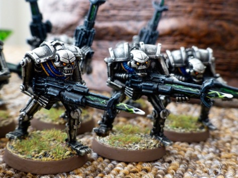Three silver coloured metal robots in the shape of skeletons armed with black rifles crackling with white green energy