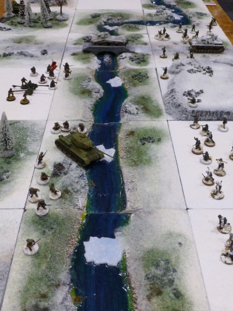 Infantry and tanks facing each other across a river in a snowy landscape
