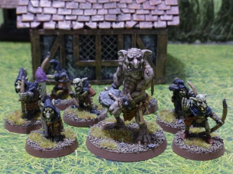 Groups of goblin archers, shaman and a large troll in front of a medieval hovel