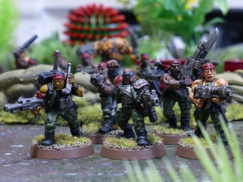 Squad of five soldiers in green uniforms and red bandanas amongst jungle plants
