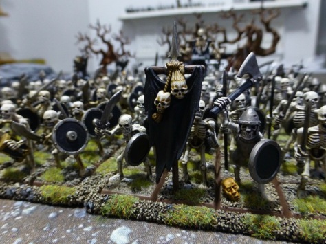 Close up view of skeleton warriors marching under a black banner hung with skull trophies
