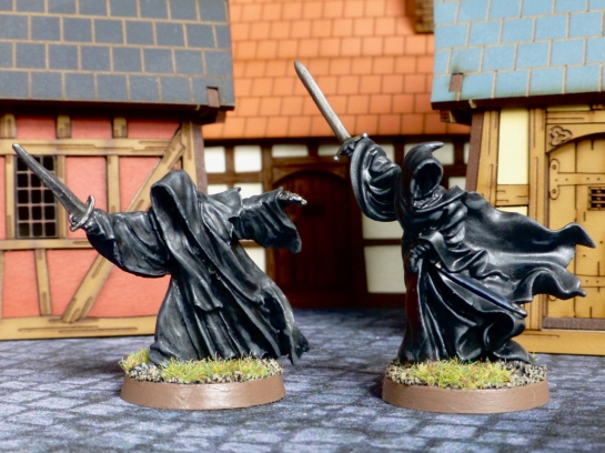 Two black cloaked figures with swords amongst medieval buildings